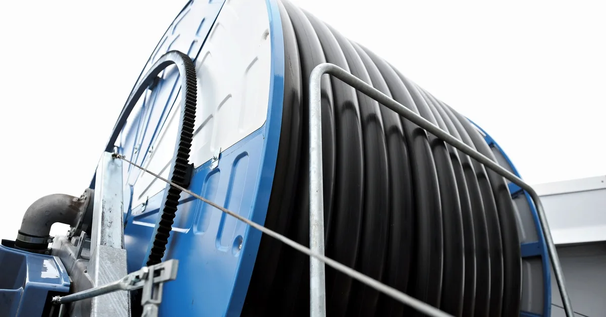 A ground-up close-up view of an industrial irrigation hose on a blue hose reel piece of equipment.